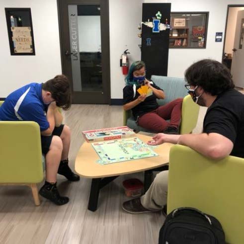 Three students sit around a table playing Monopoly in the I-Create lab