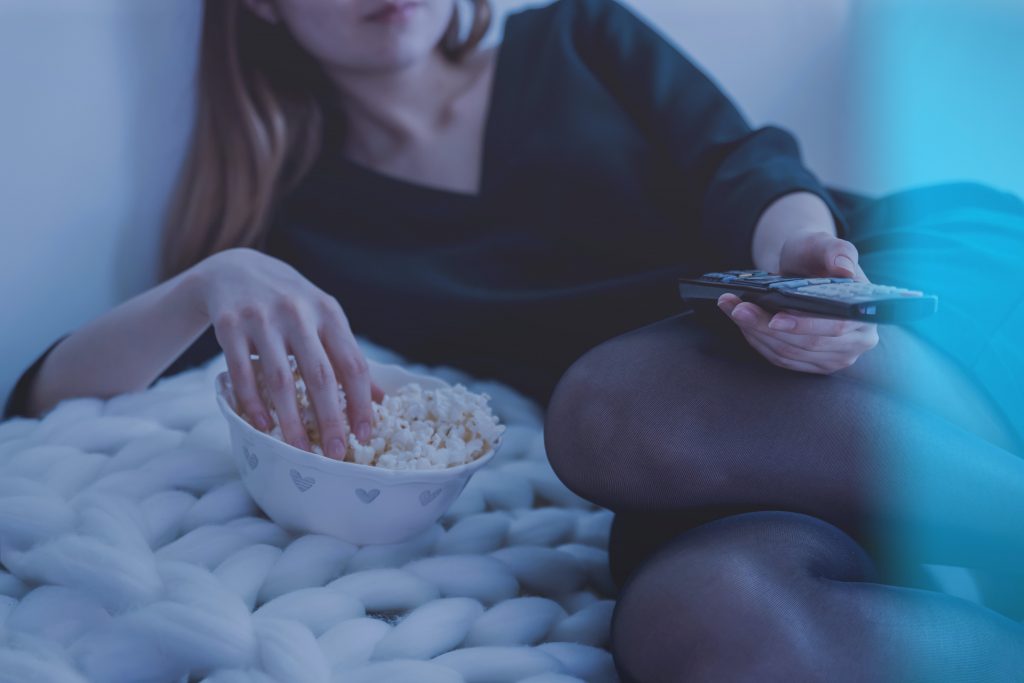 Person in bed with popcorn and television remote