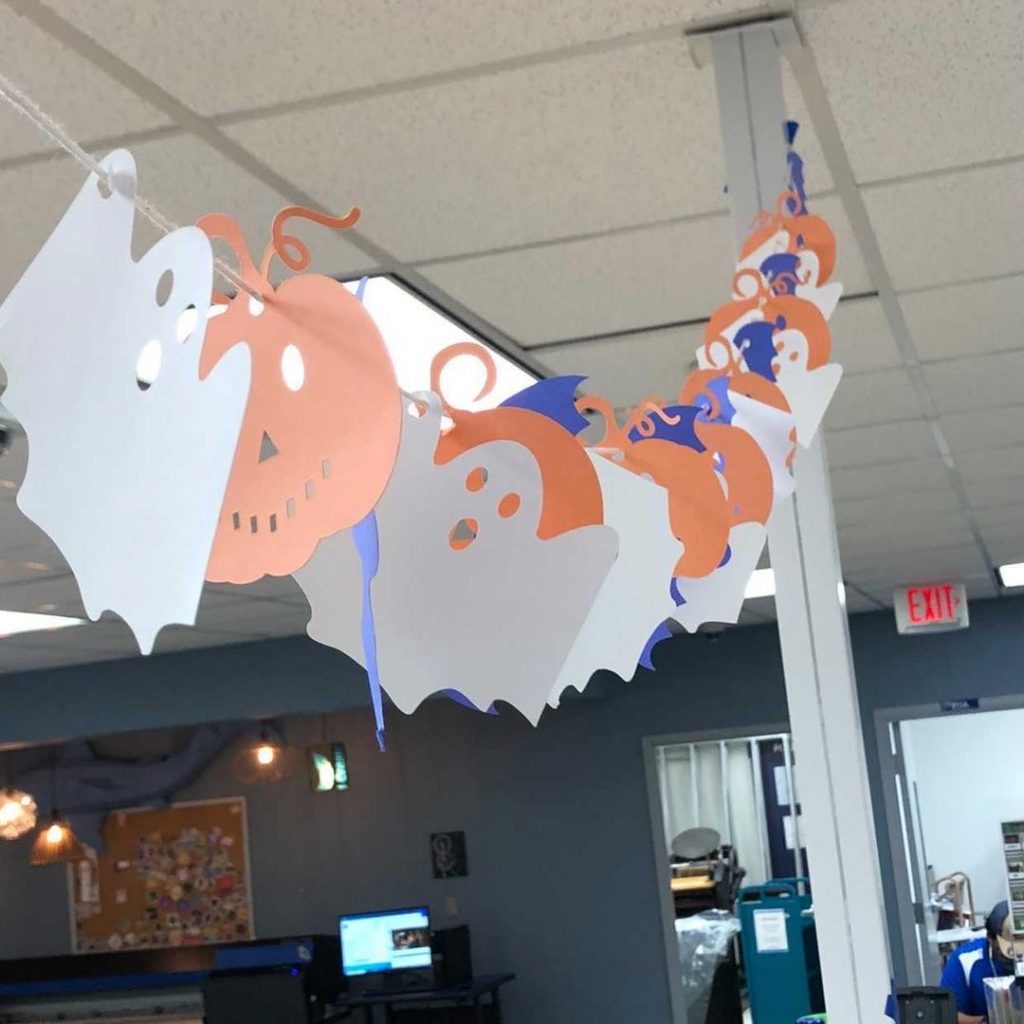 Image of a string with paper cut-outs of ghosts, pumpkins, and bats hung in the I-Create Lab. 
